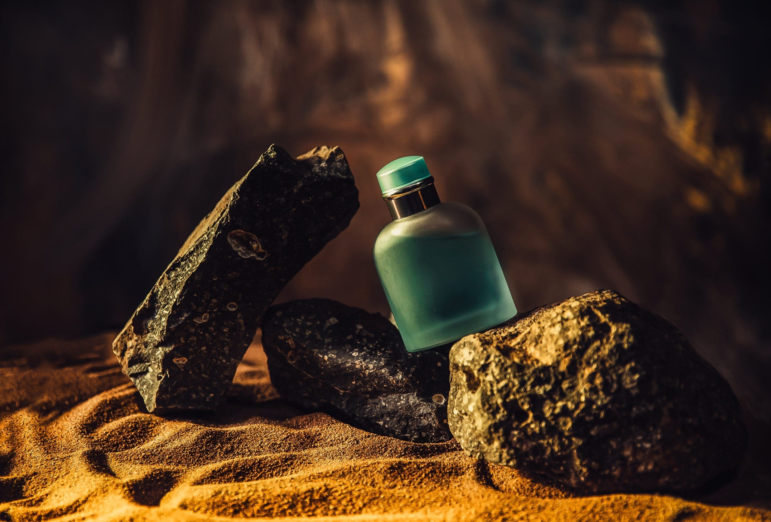 blue-perfume-bottle-with-dark-rocks-on-sand-2026-03-18-12-12-04-utc